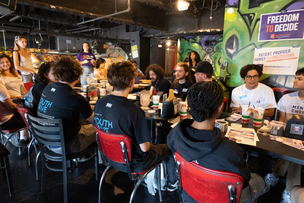 Large group of yes on prop 139 Arizona Abortion Access volunteers sitting at a long table at Spinelli's Pizza in Tempe, AZ