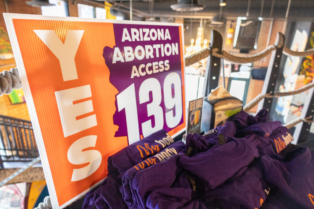 A yes on prop 139 Arizona Abortion Access yard sign set up on a table near a balcony with purple My Body, My Decision t-shirts at Spinelli's Pizza in Tempe, AZ