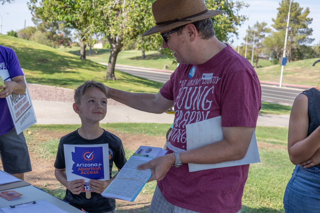 An adult man patting a young boy on the head as they're gathering materials to canvass near Kiwanis Park in Tempe, AZ for yes on 139 Arizona Abortion Access