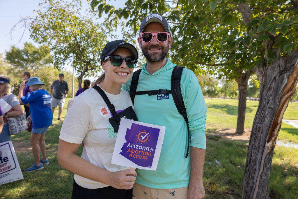 A couple standing in Kiwanis Park in Tempe, AZ holding an Arizona Abortion Access sign ready for canvass for yes on prop 139