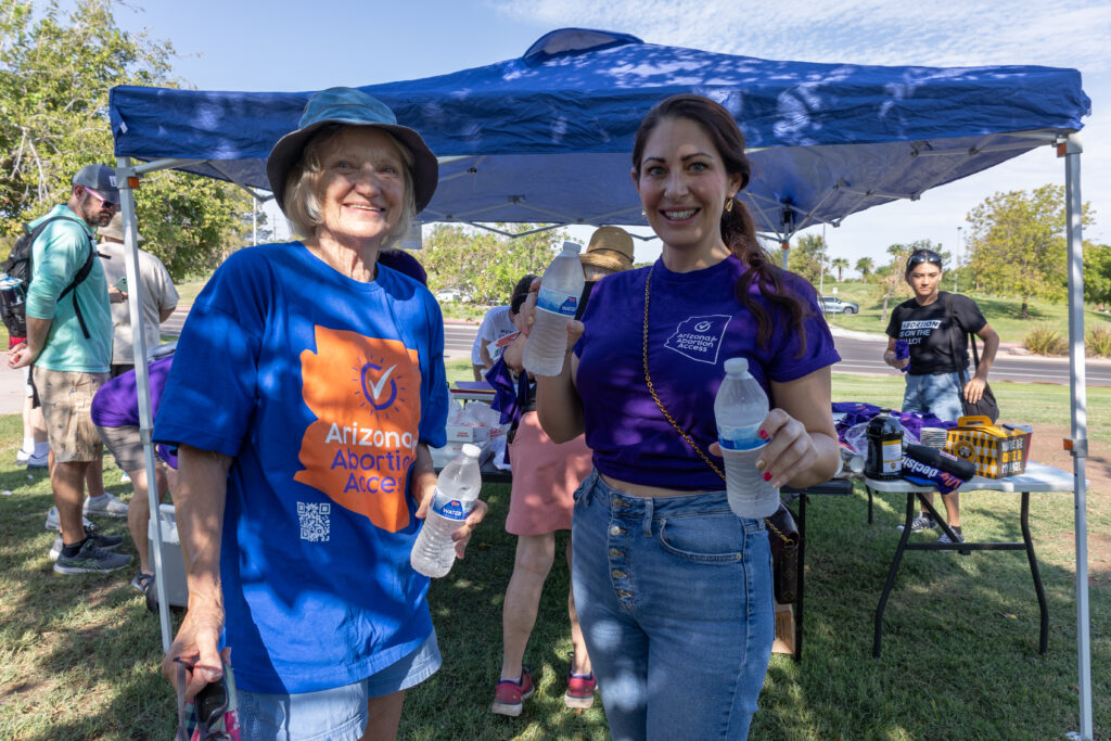 Two Arizona Abortion Access volunteers trying to keep people cool under at tent with cold water at Kiwanis Park in Tempe, AZ before canvassing for yes on prop 139