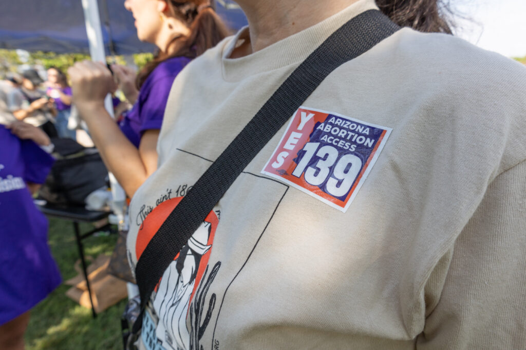 Closeup of a woman wearing an Arizona Abortion Access t-shirt with a yes on prop 139 sticker on her shoulder