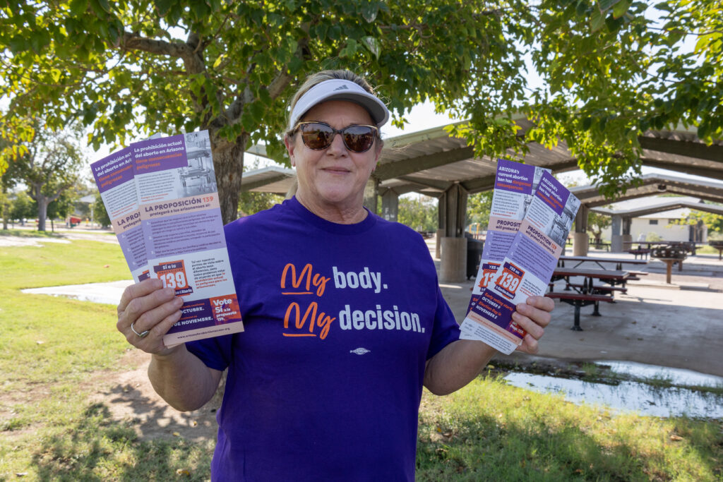 A woman holding up yes on prop 139 literature wearing a purple My Body, My Decision t-shirt ready to canvass near Kiwanis Park in Tempe, AZ