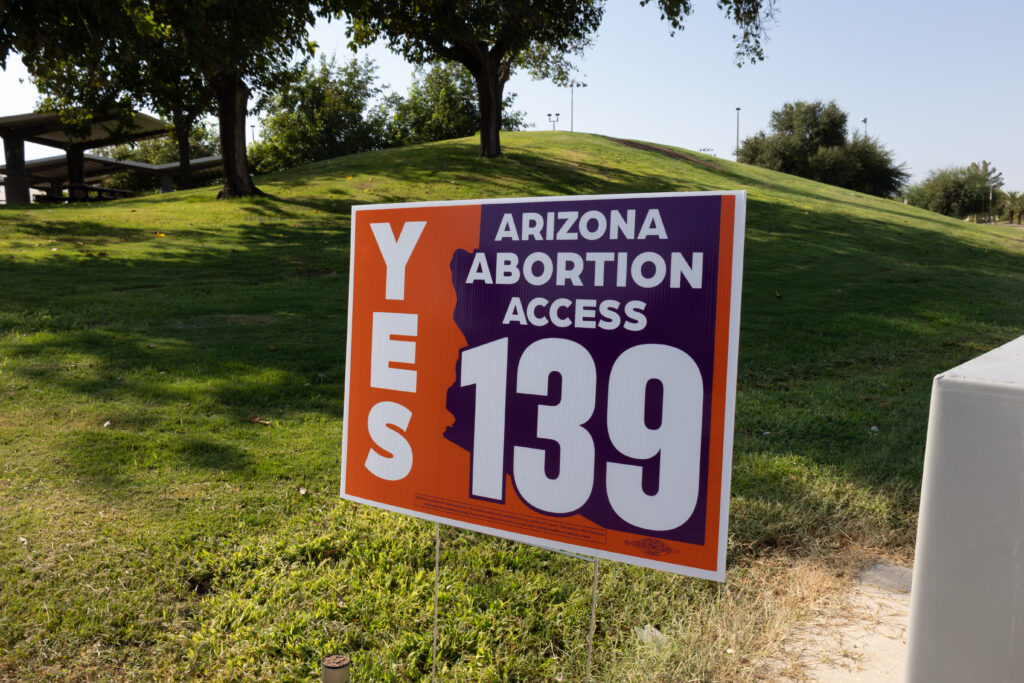 View of a yes on prop 139 Arizona Abortion Access yard sign in front of a tree lines hill at Kiwanis Park in Tempe, AZ