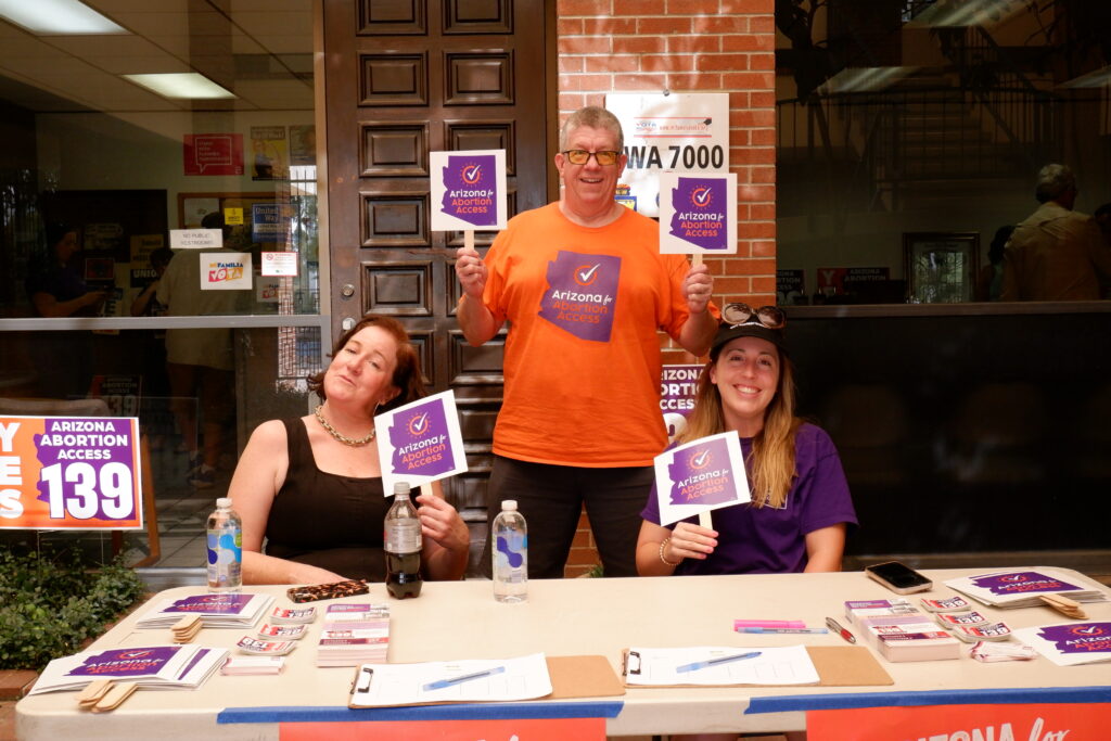 A group of three Arizona Abortion Access volunteers tabling for yes on prop 139 posing with signs in Tucson